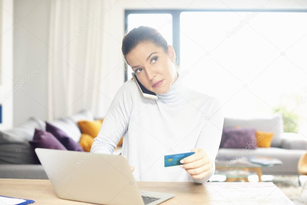 Attractive woman using her laptop to make online purchases with her credit card while sitting at desk at home.