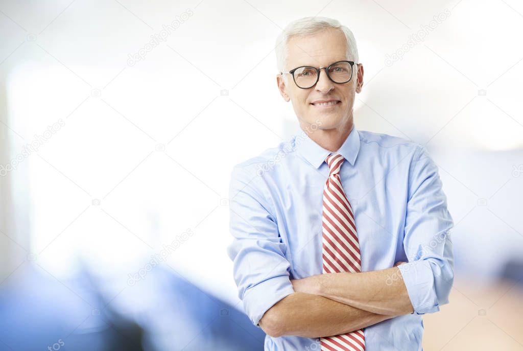 Mature happy buisnessman standing with arms crossed while looking at camera and smiling.