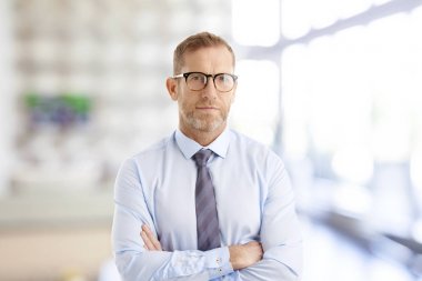 Portrait of middle aged businessman wearing shirt and tie while standing with arms crossed at the office. clipart