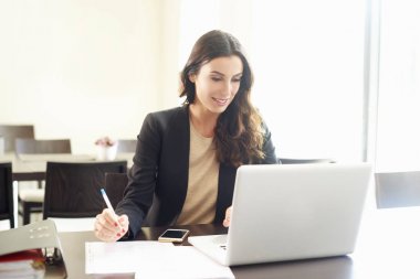 Dizüstü bilgisayar kullanarak ve dizüstü bilgisayarda çalışırken biraz evrak işi yapıyor güzel genç iş kadını.