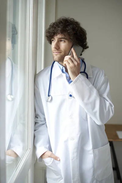 Young male doctor using mobile phone while talking with his patient.