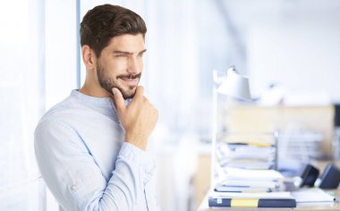 Yakışıklı bir delikanlı ile portre çekim ofiste ayakta ve onun iş fikri hakkında düşünme çene el.