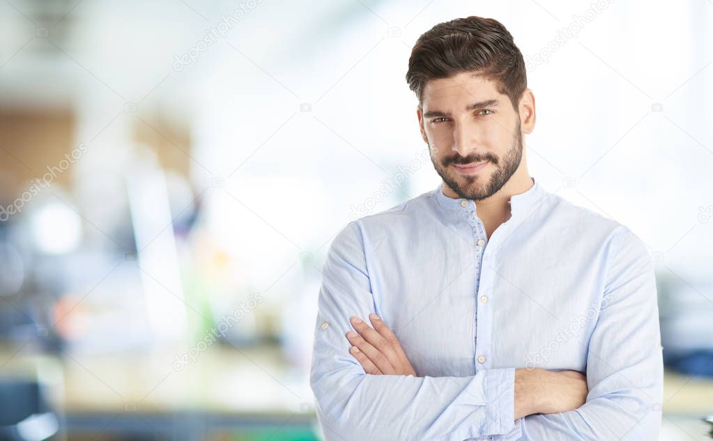Portrait of a young businessman standing with arms crossed at the office. 