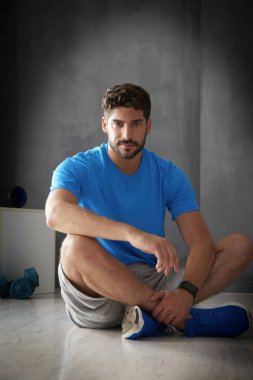 Salonda oturan ve rahatlatıcı bir genç erkek kişisel antrenör tam uzunlukta portresi. 
