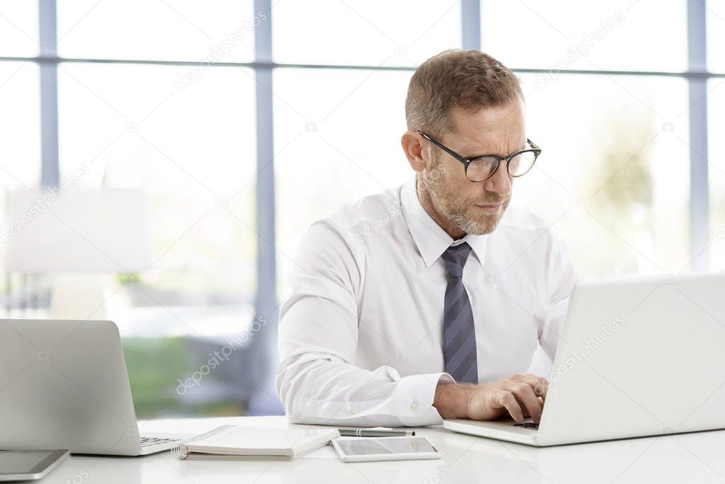 Careworn financial advisor businessman wearing shirt and tie whilw sitting at desk in front of laptop and working at the office. 