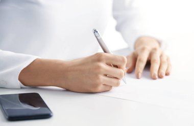 Kalem tutan ve ofis masa başında otururken bir şey not defterine yazma işkadını'nın el yakın çekim shot.