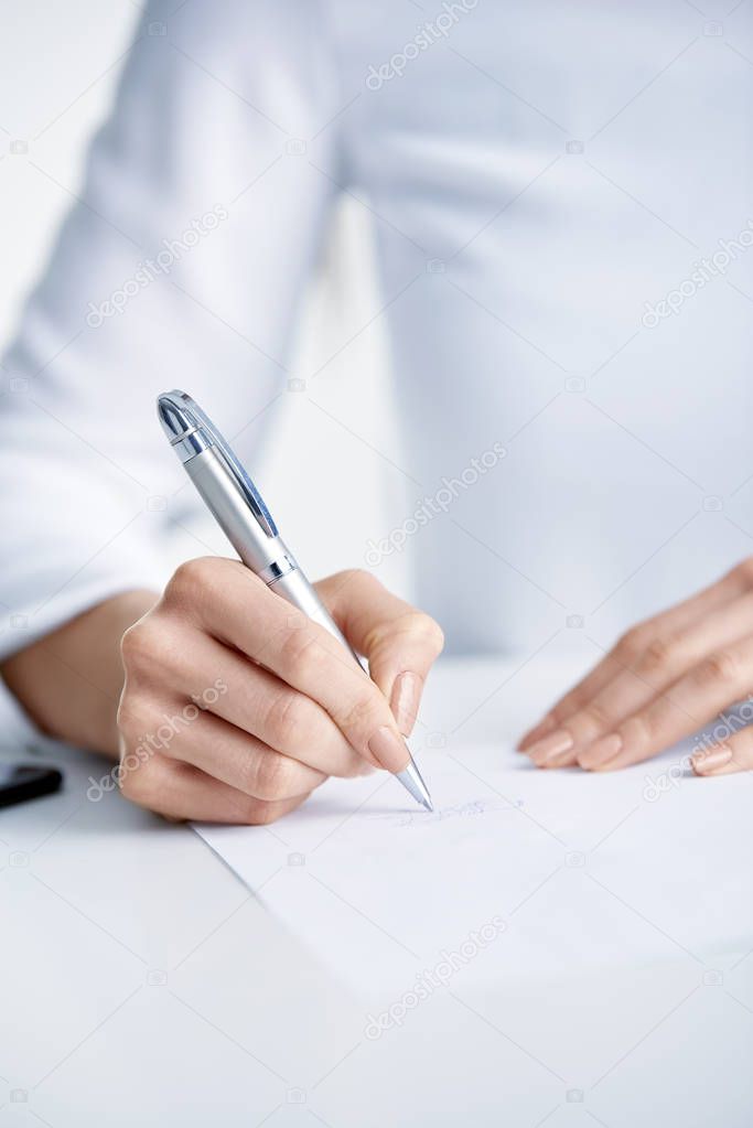 Close-up shot of businesswoman's hand holding pen and sign the paper while sitting at office desk.