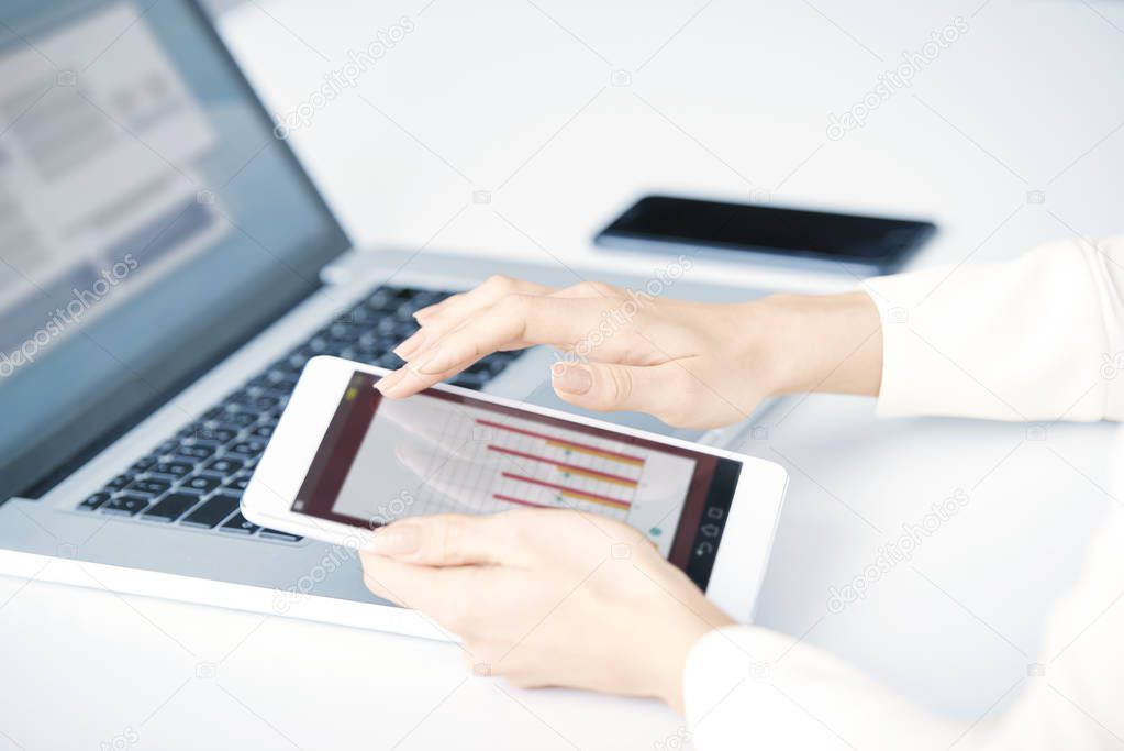 Close-up of businesswoman's hand using digital tablet and analyzing financial data while sitting in front of laptop at office desk and working on new business report. Isolated on white background. 