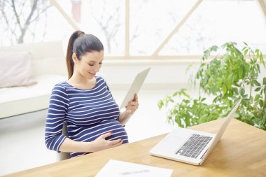 Dijital tablet kullanma ve browsing belgili tanımlık enterne evde otururken mutlu genç kadın. 