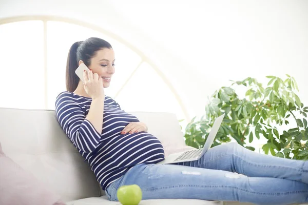 그녀의 전화에 집에서 노트북을 임신한 여자의 초상화 — 스톡 사진
