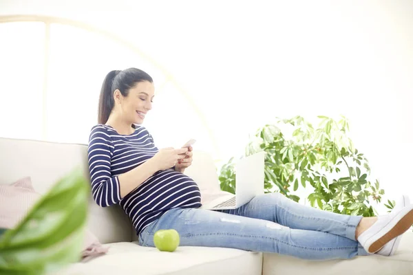그녀의 전화에 메시징 집에서 노트북을 임신한 텍스트의 초상화 — 스톡 사진