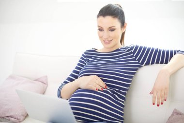 Gülümseyen dizüstü kullanarak ve browsing belgili tanımlık enterne evde kanepede otururken hamile kadın. 