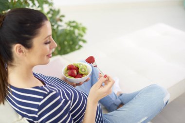 Yüksek açı çekim evde rahatlatıcı ve bir tabak meyve salatası yemek güzel hamile kadın.