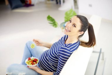 Yüksek açı çekim evde rahatlatıcı ve bir tabak meyve salatası yemek güzel hamile kadın.