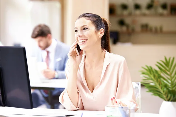 Geschäftsfrau SMS, während sie am Schreibtisch sitzt — Stockfoto