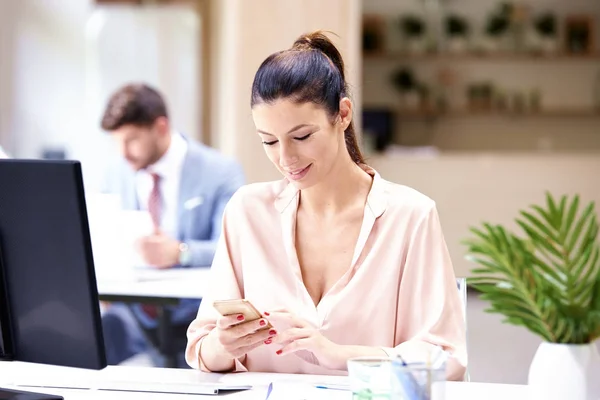 Podnikatelka dostávající textové zprávy během sezení na kancelářském stole — Stock fotografie