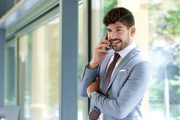 Executive businessman standing at the window in the office and t — Stock Photo, Image