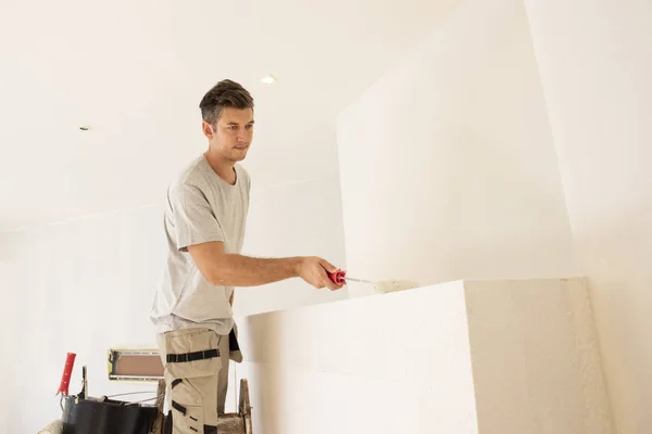 Młody mężczyzna maluje ścianę w mieszkaniu — Zdjęcie stockowe