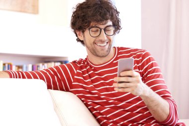 Portrait shot of handsome young man text messaging while relaxing on the sofa at home. 