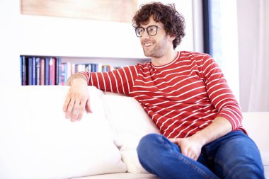 Evdeki kanepede dinlenirken günlük giysiler ve gözlük giyen mutlu bir adamın portresi..