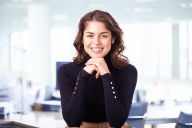 Kendine güvenen genç iş kadını kameraya bakıyor ve gülümsüyor.