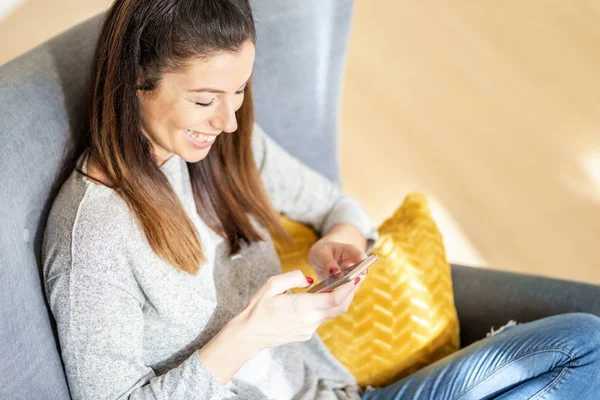 Mujer feliz usando su teléfono móvil y mensajes de texto mientras se sienta — Foto de Stock