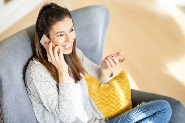 Boldog nő telefonál, miközben otthon ül. — Stock Fotó