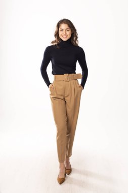 Kapalı alanda poz verirken balıkçı yaka kazak ve pantolon giyen çekici genç bir kadın.. 