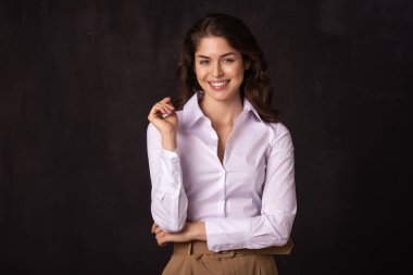 Beyaz gömlek giyen ve arka planda durup gülen çekici bir genç kadının portresi.. 