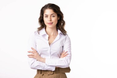 Çekici genç iş kadınının portre resmi. Beyaz gömlek giymiş ve kollarını kavuşturmuş beyaz arka planda dururken gülümsüyor..