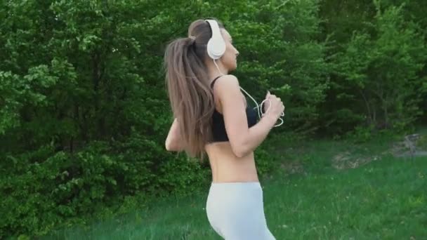 Дівчина в навушниках біжить — стокове відео