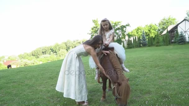 Madre enrolla a su hija en un pony — Vídeos de Stock