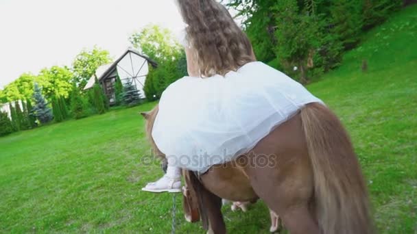 Madre enrolla a su hija en un pony — Vídeo de stock