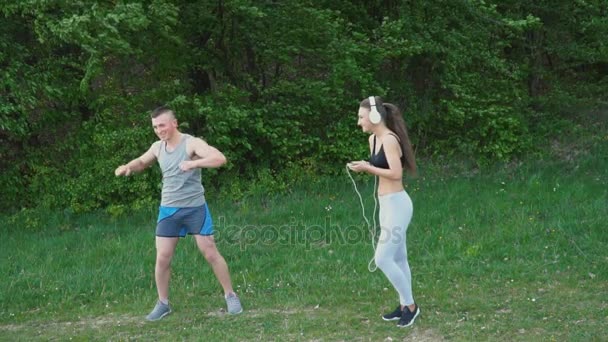 El tipo hace el calentamiento mientras la chica lleva auriculares. — Vídeo de stock