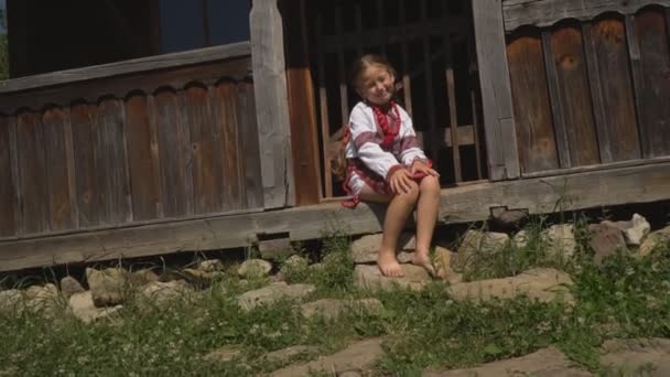Bambina è seduta sotto il portico della casa — Video Stock
