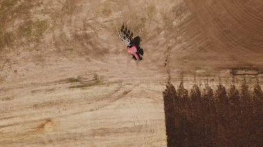 Kırmızı bir traktör tarlayı sürüyor.