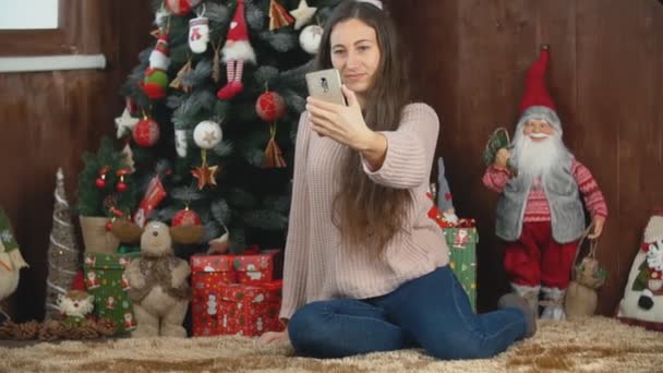 Ragazza fa selfie mentre seduto vicino all'albero di Natale — Video Stock