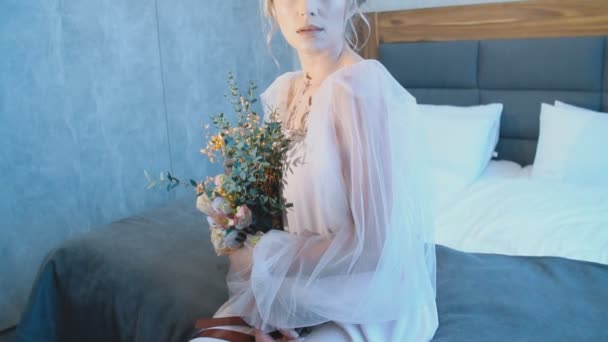 Дівчина з букетом квітів, що сидить на ліжку — стокове відео