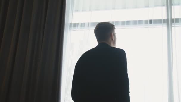 Ένας άντρας στέκεται και κοιτάει έξω από το παράθυρο. — Αρχείο Βίντεο