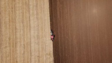 Kırmızı bir traktör tarlayı sürüyor.