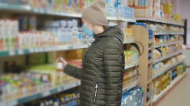 Tıp maskeli kadın süpermarkette sıraların arasında yürüyor.