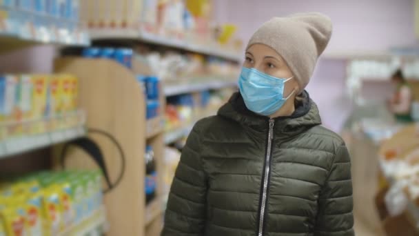 Жінка в медичній масці ходить між рядами в супермаркеті — стокове відео