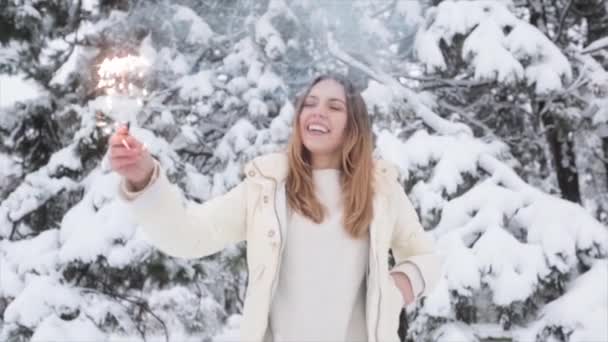 Joven chica positiva en el bosque de invierno nevado. Navidad y chispas — Vídeo de stock