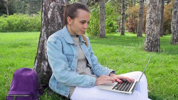 Молода дівчина сидить поза офісною будівлею працює на ноутбуці — стокове відео