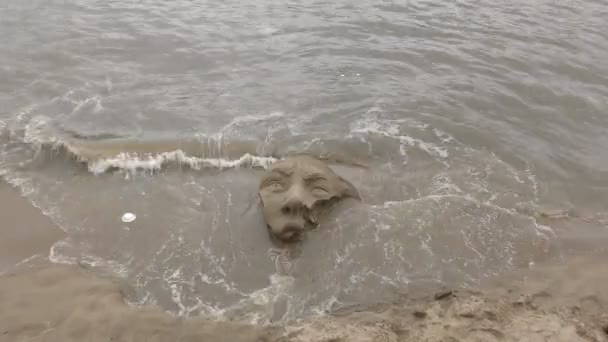 Wellen spülen die Sandstatue vom Gesicht. — Stockvideo