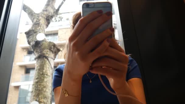 Eine Frau mit einem Handy am Fenster. — Stockvideo
