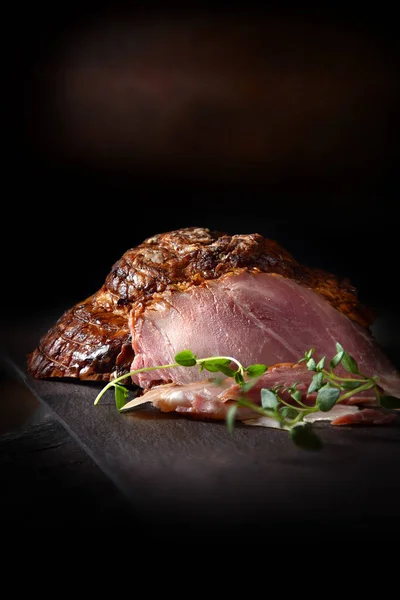 Prime honey roasted ham joint, carved and ready to serve with thyme herb garnish. Shot against a rustic background with accommodation for copy space.