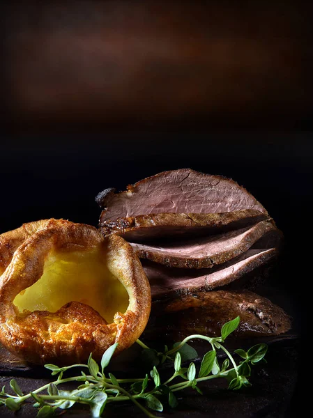 Traditional Sunday roast lunch, prime roast beef with Yorkshire puddings and thyme garnish shot against a rustic background with copy space.