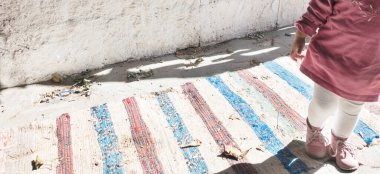 Panorama manzarası küçük kız bacağı ve küçük ayakkabılar çizgili halı üzerinde duruyor..