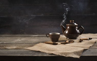 Bir fincan sıcak sıcak çaydanlık ve tarçın çubuğu ve ahşap tahta üzerinde anason yıldızı. Kopyalama alanı olan eski arkaplan.